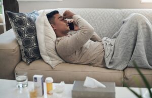 Shot of a young man talking on a cellphone while feeling sick at home